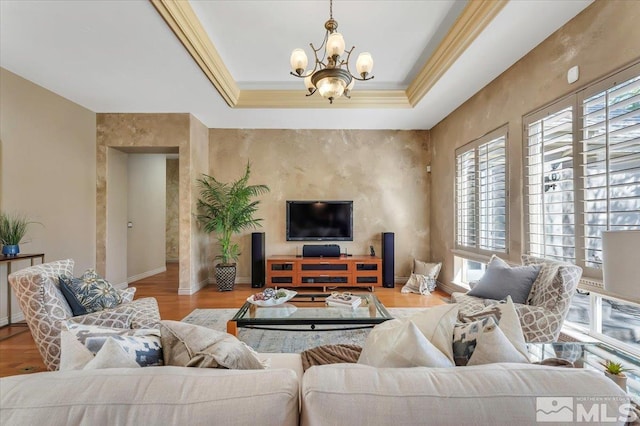 living room with a raised ceiling, light hardwood / wood-style floors, crown molding, and a notable chandelier