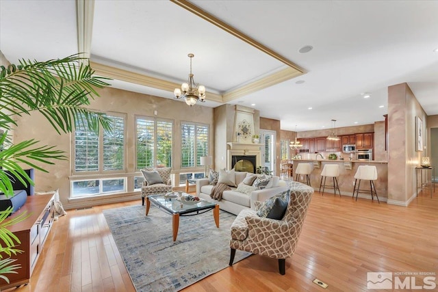 living room with an inviting chandelier, light wood-type flooring, a raised ceiling, and a large fireplace