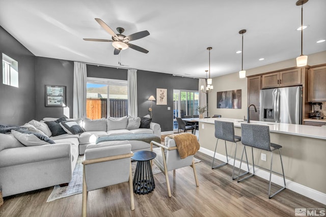 living room featuring ceiling fan with notable chandelier, light hardwood / wood-style floors, and a wealth of natural light