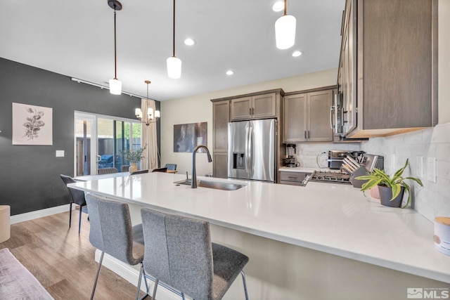 kitchen featuring pendant lighting, light wood-type flooring, sink, a kitchen breakfast bar, and appliances with stainless steel finishes