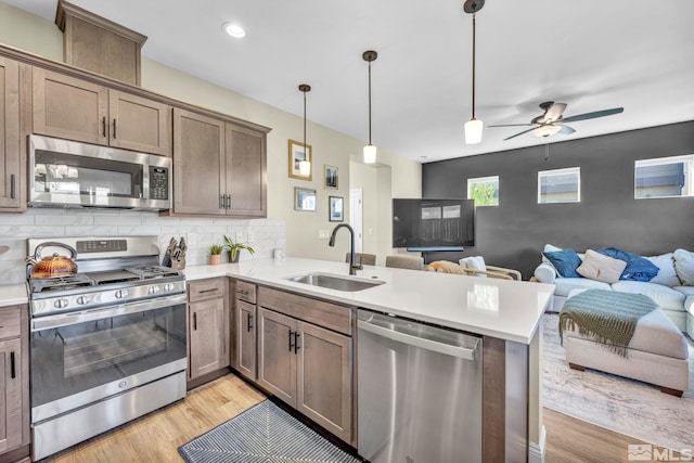 kitchen with hanging light fixtures, sink, kitchen peninsula, light hardwood / wood-style flooring, and appliances with stainless steel finishes