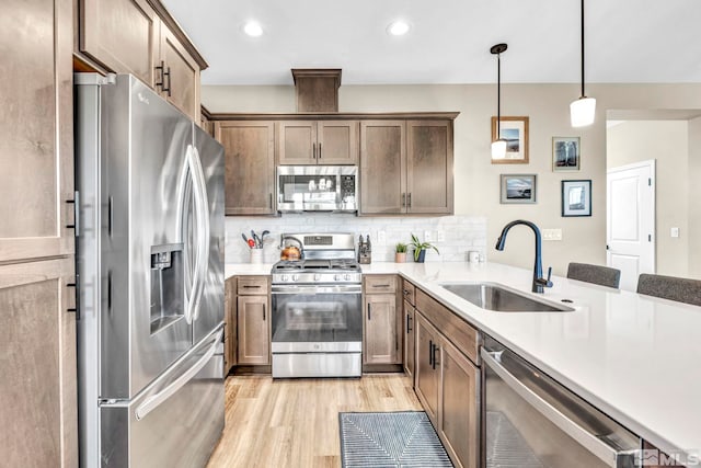 kitchen with appliances with stainless steel finishes, hanging light fixtures, tasteful backsplash, light wood-type flooring, and sink