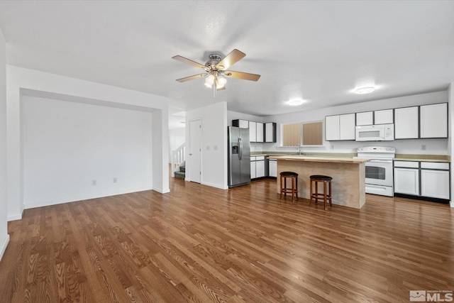 kitchen with white cabinets, white appliances, wood-type flooring, and a breakfast bar area