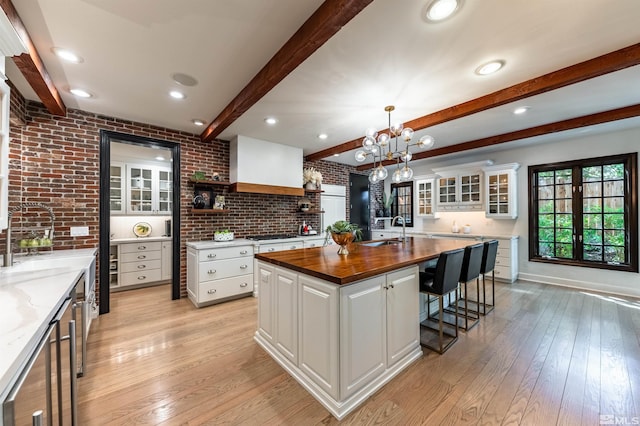 kitchen with white cabinets, beamed ceiling, wood counters, and a kitchen island with sink