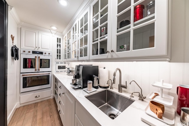 kitchen with light stone counters, white cabinets, light wood-type flooring, multiple ovens, and sink