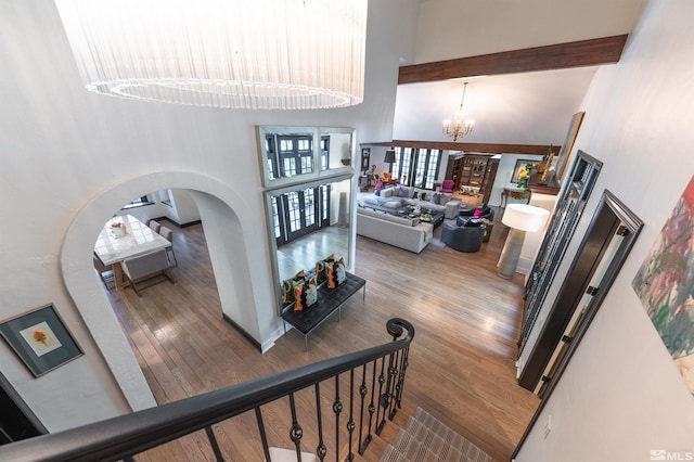 stairs with a high ceiling, beam ceiling, hardwood / wood-style floors, and a notable chandelier