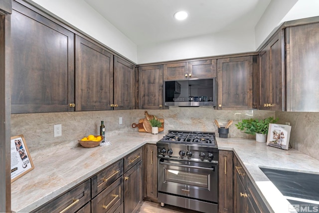 kitchen featuring dark brown cabinetry, backsplash, stainless steel appliances, and light stone counters