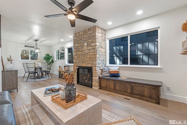 living room with ceiling fan, a stone fireplace, and light wood-type flooring