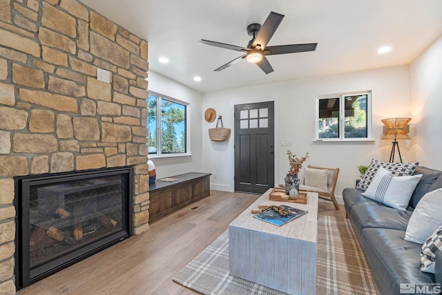 living room featuring ceiling fan, a stone fireplace, and hardwood / wood-style flooring