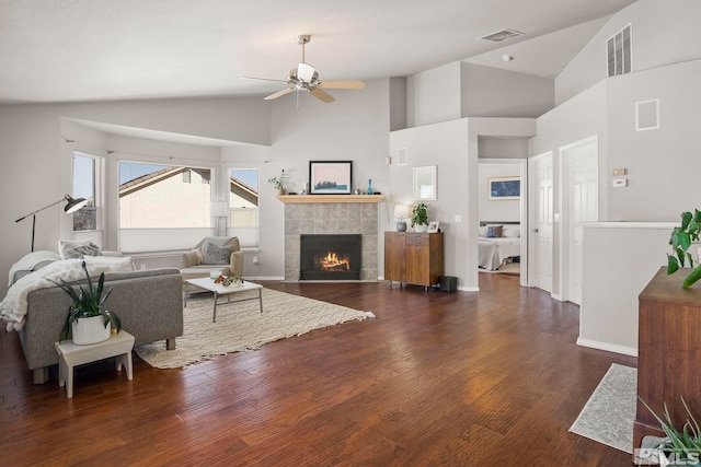 living room with ceiling fan, dark hardwood / wood-style floors, a tiled fireplace, and high vaulted ceiling