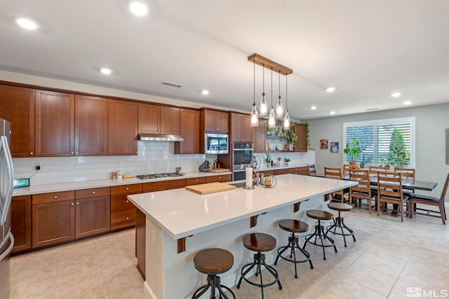 kitchen with pendant lighting, tasteful backsplash, a breakfast bar area, a center island with sink, and appliances with stainless steel finishes