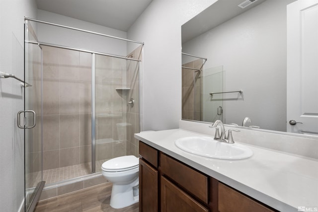 bathroom with wood-type flooring, vanity, a shower with shower door, and toilet