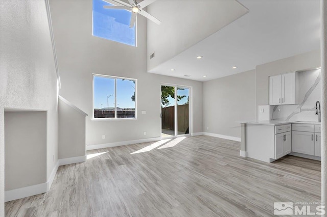 unfurnished living room featuring ceiling fan, light hardwood / wood-style flooring, and a towering ceiling