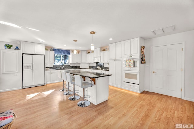 kitchen with white cabinets, white appliances, a kitchen island, light hardwood / wood-style flooring, and decorative light fixtures