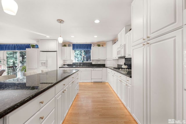 kitchen with dark stone countertops, white cabinetry, white appliances, light wood-type flooring, and decorative light fixtures