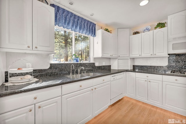 kitchen featuring white cabinets, white appliances, light wood-type flooring, dark stone counters, and sink