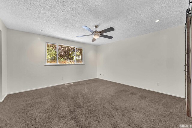 carpeted empty room featuring ceiling fan, a barn door, and a textured ceiling