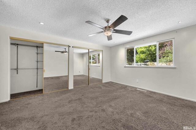 unfurnished bedroom with ceiling fan, multiple closets, a textured ceiling, and dark colored carpet