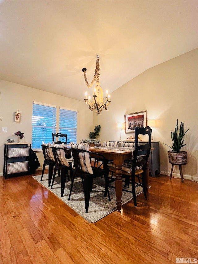 dining room with hardwood / wood-style flooring, a chandelier, and vaulted ceiling