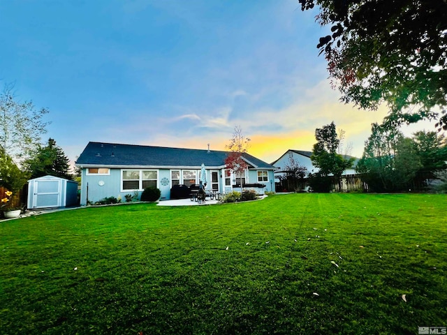 back house at dusk featuring a storage unit, a patio area, and a yard