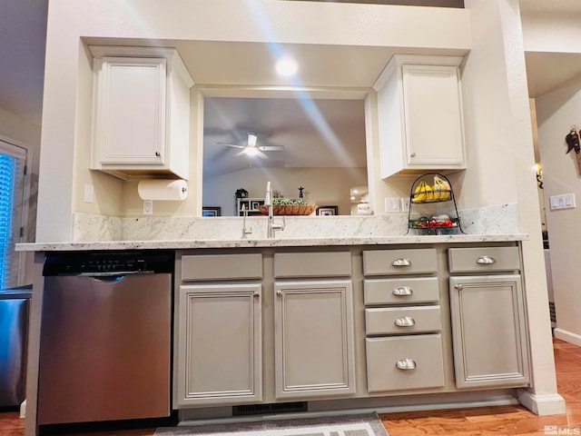 kitchen with light stone counters, light wood-type flooring, sink, and stainless steel dishwasher