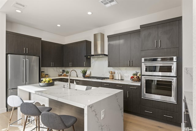 kitchen with a sink, wall chimney exhaust hood, a breakfast bar, appliances with stainless steel finishes, and visible vents