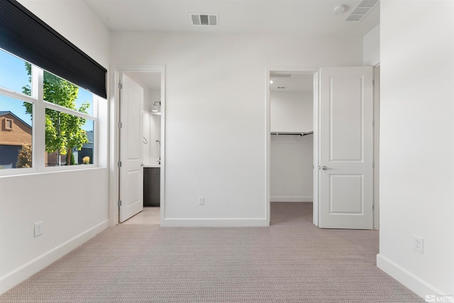 unfurnished bedroom featuring a spacious closet, connected bathroom, a closet, and light carpet