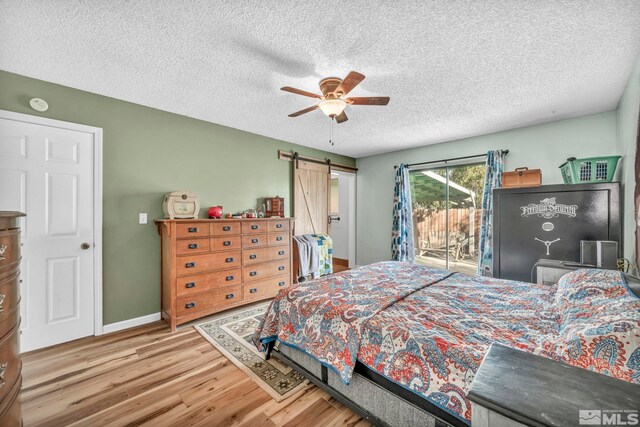 bedroom featuring ceiling fan, access to exterior, a textured ceiling, light hardwood / wood-style flooring, and a barn door