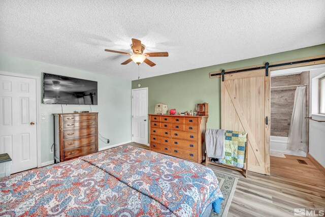 bedroom featuring a textured ceiling, a barn door, connected bathroom, ceiling fan, and light wood-type flooring