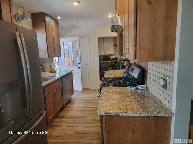 kitchen with appliances with stainless steel finishes, backsplash, independent washer and dryer, ventilation hood, and light wood-type flooring