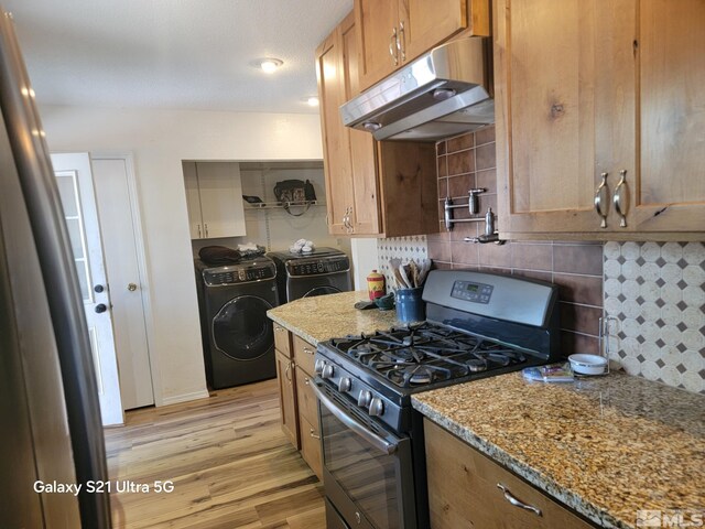 kitchen with light stone counters, separate washer and dryer, backsplash, stainless steel gas range, and light hardwood / wood-style floors