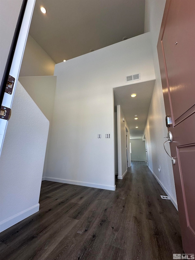 hallway with a towering ceiling and dark wood-type flooring