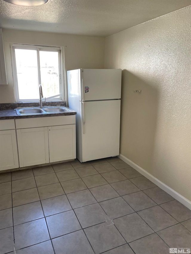 kitchen with white cabinetry, a textured ceiling, white fridge, and sink