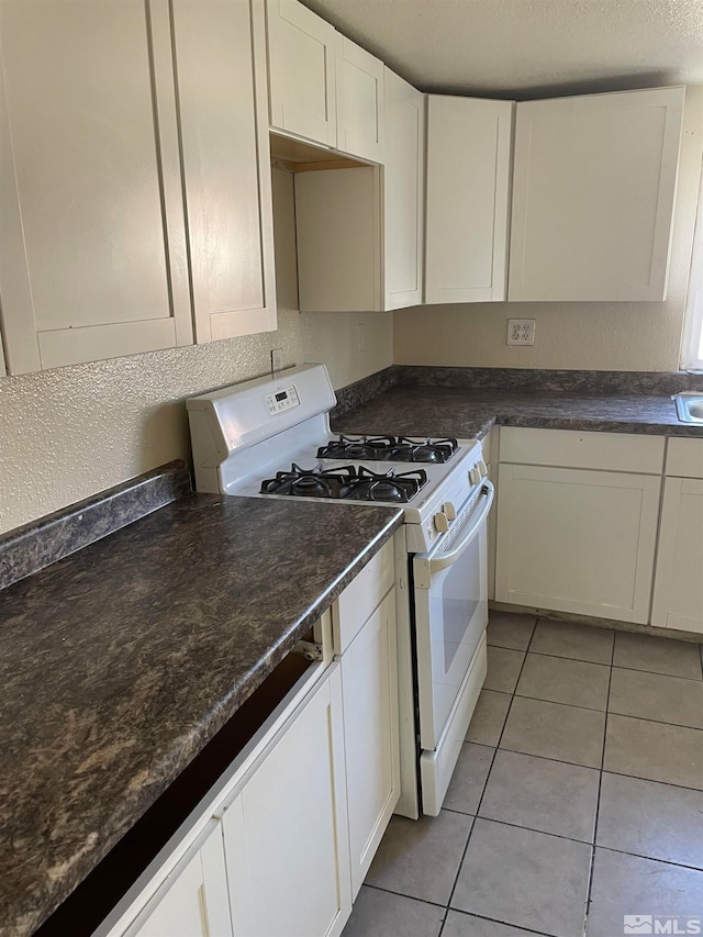 kitchen featuring white range with gas cooktop, light tile patterned floors, and white cabinets