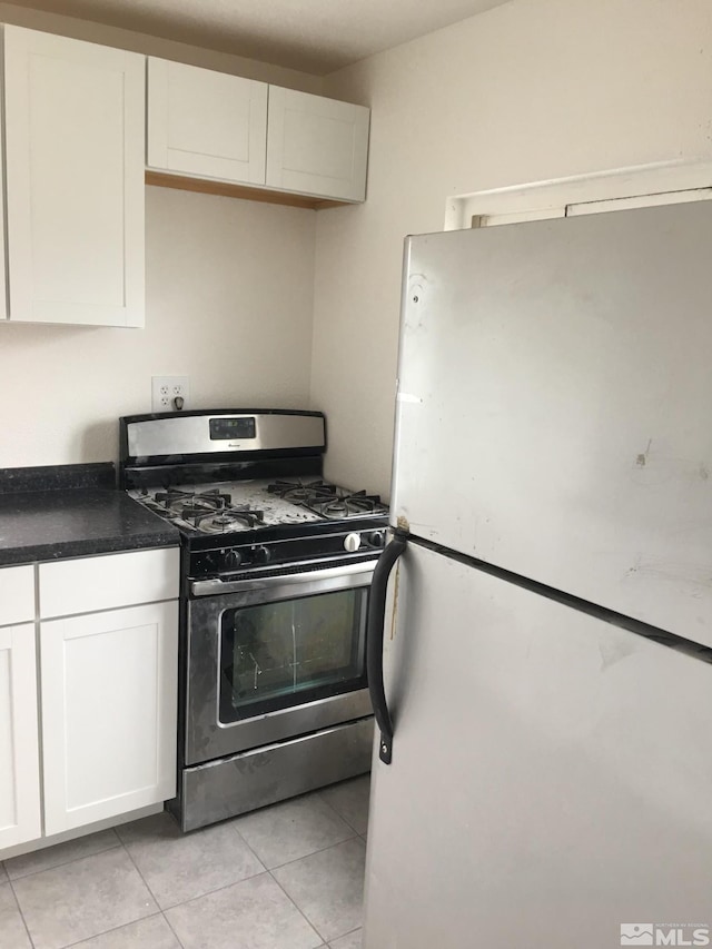 kitchen with light tile patterned floors, white cabinets, white fridge, and stainless steel range with gas stovetop