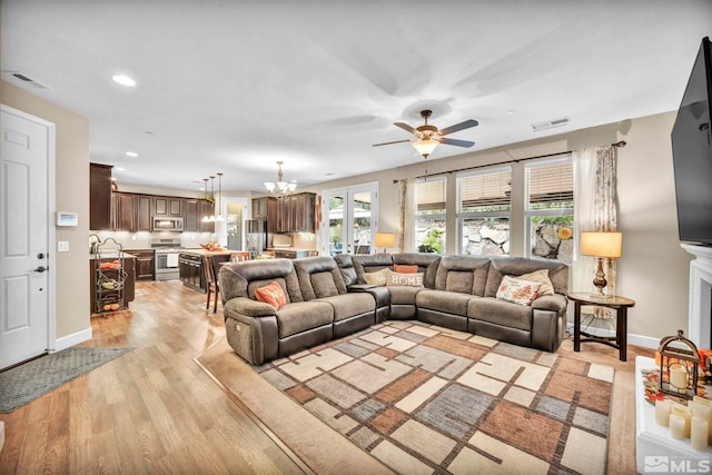 living room with ceiling fan with notable chandelier and light hardwood / wood-style floors