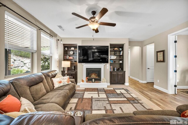 living room featuring light hardwood / wood-style floors, ceiling fan, and built in shelves