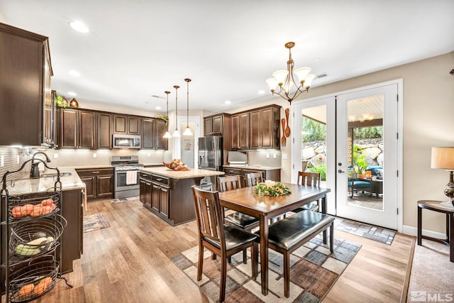 kitchen with hanging light fixtures, a kitchen island, dark brown cabinets, appliances with stainless steel finishes, and light hardwood / wood-style floors