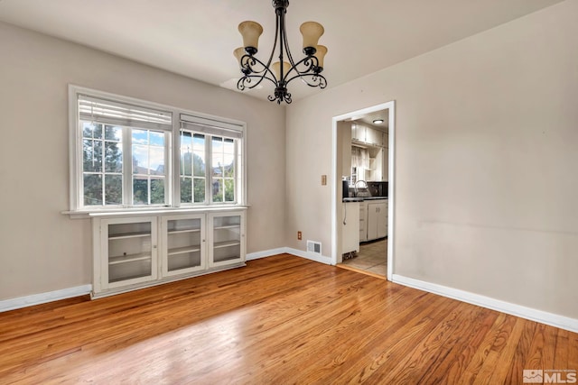 unfurnished dining area featuring sink, a chandelier, and light hardwood / wood-style floors