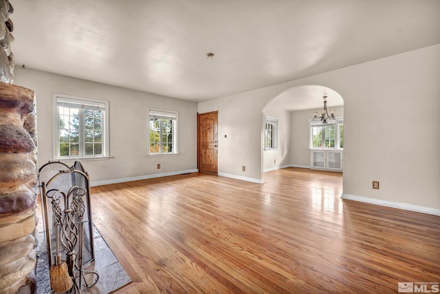 unfurnished living room with an inviting chandelier, a wealth of natural light, and light wood-type flooring