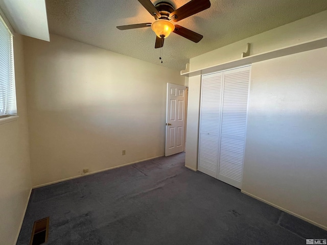 unfurnished bedroom featuring dark colored carpet, a closet, ceiling fan, and a textured ceiling