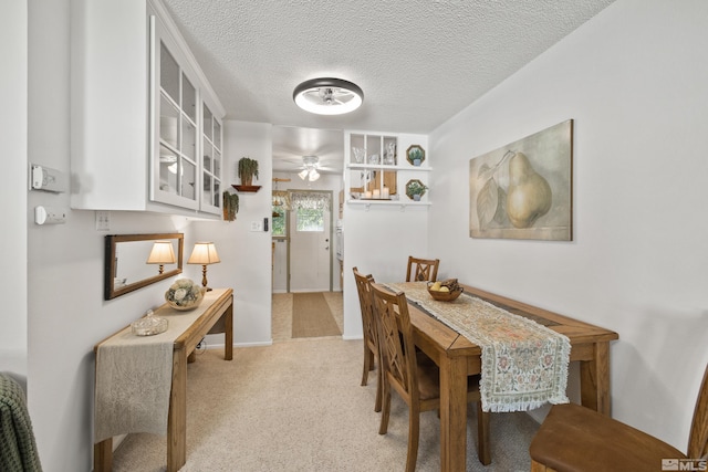 dining room with a textured ceiling, light colored carpet, and ceiling fan