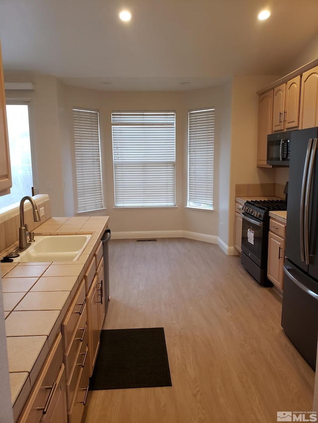 kitchen featuring black appliances, sink, light hardwood / wood-style flooring, light brown cabinetry, and tile counters