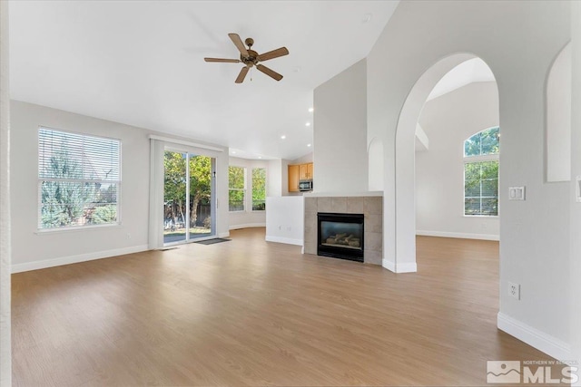 unfurnished living room with ceiling fan, high vaulted ceiling, a tiled fireplace, and light hardwood / wood-style floors