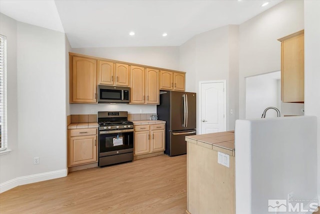 kitchen with light wood-type flooring, light brown cabinets, tile counters, lofted ceiling, and appliances with stainless steel finishes