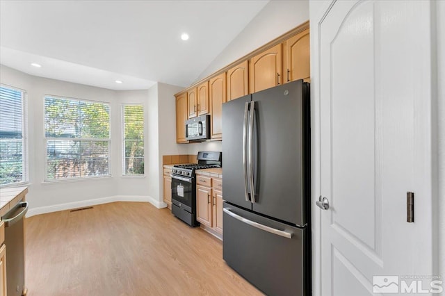 kitchen featuring appliances with stainless steel finishes, light brown cabinetry, vaulted ceiling, and light hardwood / wood-style floors