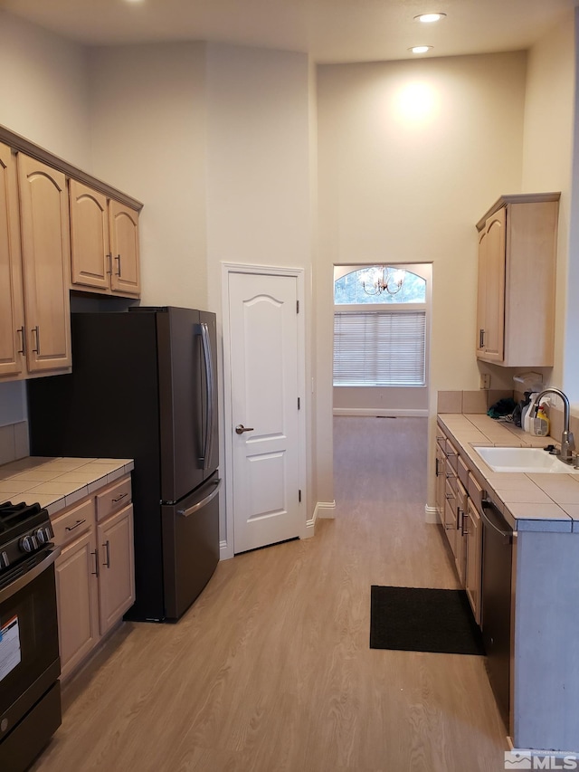 kitchen with stainless steel appliances, sink, light wood-type flooring, and tile counters