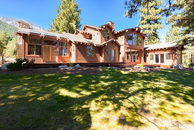 rear view of property featuring a deck with mountain view and a lawn