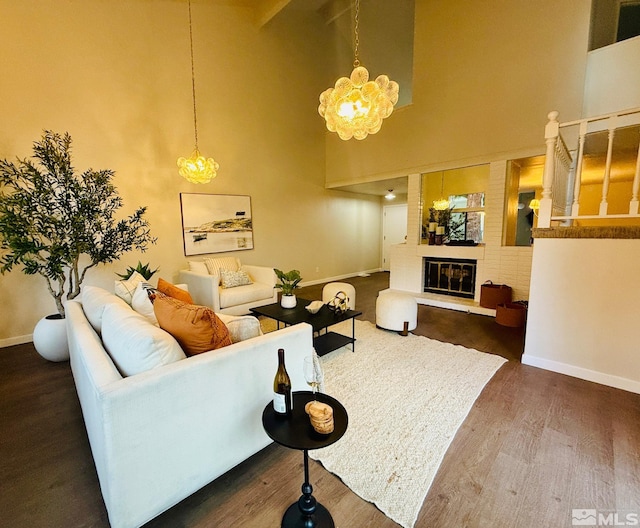 living room featuring a high ceiling, a brick fireplace, dark hardwood / wood-style floors, and a chandelier