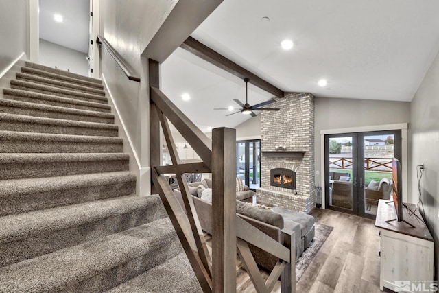 stairway featuring a brick fireplace, ceiling fan, hardwood / wood-style floors, beam ceiling, and french doors